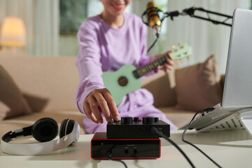 Closeup image of teenage girl turning up volume on amplifier when recording herself playing ukulele
