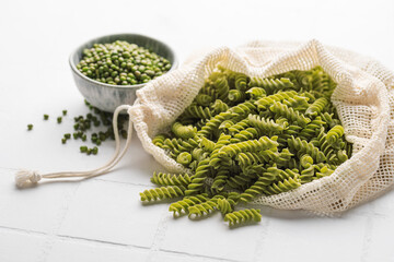 Fusilli green mung bean pasta on a white tile background.