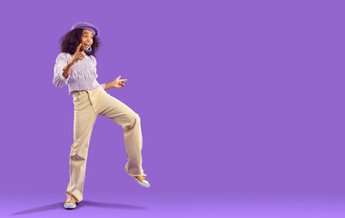 Fototapeta na wymiar Overjoyed teen african american girl in funky cool clothes dance isolated on purple studio background. Funny biracial teenager have fun make dancer moves. Youth hobby and entertainment. Copy space.