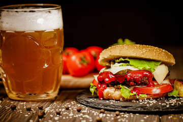 Homemade beef burger with glass of beer, tomatoes, cheese, sauce on stone board. Selective focus 