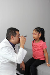 Professional specialist pediatrician doctor and patient 4-year-old Latino brown-haired girl are in consultation to check their eyes, mouth and throat to diagnose any disease in the office

