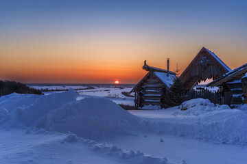 Rural landscape with snowdrifts and a log house on the high bank of the Irtysh, Siberia.