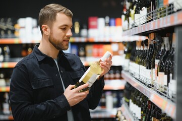 Young man looking at bottle of wine in supermarket