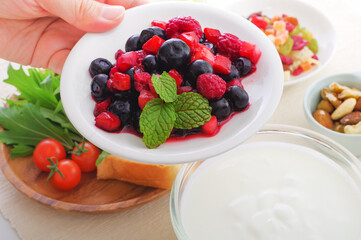 ヨーグルトにミックスベリーをトッピングする女性