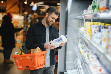 Customer In Supermarket. Man Doing Grocery Shopping Standing With Cart Choosing Food Product Indoors. Guy Buying Groceries In Food Store. Selective Focus, Copy Space.