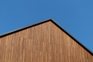 Fototapeta premium Wooden plank gabled roof on a new modern house against a blue clear sky, copy space.