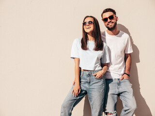 Fototapeta Smiling beautiful woman and her handsome boyfriend. Woman in casual summer jeans clothes. Happy cheerful family. Female having fun. Sexy couple posing in the street at sunny day. Near white wall obraz