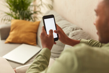 Man Using Smartphone At Home. Handsome Multiracial Guy Sitting On Sofa And Messaging In Cozy Living Room at Home. Male Person Doing Online Shopping, Browsing Internet and Checking Social Media 