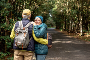 Lovely senior couple enjoying nature outdoors in a mountain forest walking in the road. Joyful...