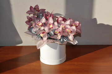 Round white box with a bouquet of orchids on a wooden background. Mockup