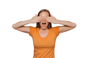 Pretty redhead  woman in orange t-shirt, closes her eyes by hands with wide open screaming mouth, prepared for surprise. Stands over transparent background. Presents and holidays. Scared woman