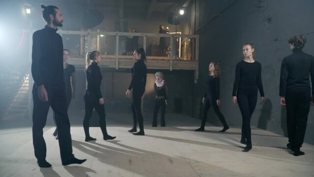 Panning shot of backstage with young actors and actresses strolling with serious facial expressions. Confident talented Caucasian men and women in black rehearsing performance in theatre