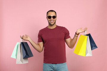 Happy African American man in sunglasses with shopping bags on pink background