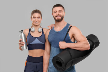 Athletic people with headphones, thermo bottle and fitness mat on grey background