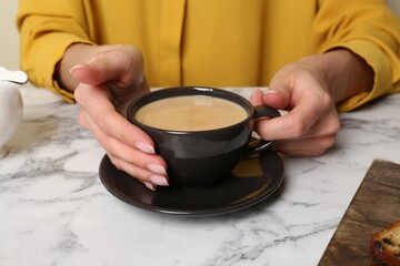 Woman with cup of aromatic coffee at white marble table, closeup