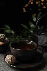 Obraz na płótnie Canvas Cup of aromatic tea and delicious vegan candy ball on grey table against blurred lights, space for text