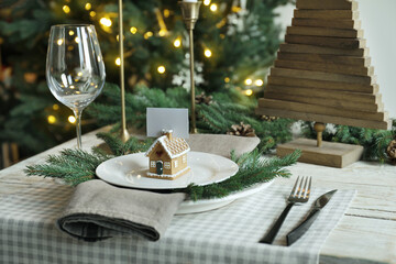 Festive place setting with beautiful dishware, cutlery and gingerbread house card holder for Christmas dinner on wooden table