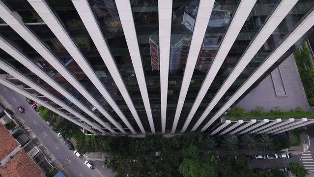 Drone flying up, near a simetrical mirrored building, camera pointing down revealing the building as it goes up