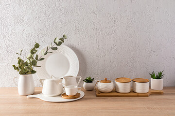 Beautiful kitchen background with various white utensils and indoor flowers in pots. wooden table top. Grey textured wall with space for your text.
