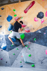 Obraz na płótnie Canvas One Rock climber man hanging on a bouldering climbing wall, inside on colored hooks.