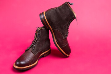 Pair of Premium Dark Brown Grain Brogue Derby Boots Made of Calf Leather with Rubber Sole Placed Over One Another On Pink Background.