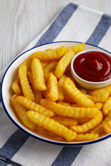 Homemade Unhealthy Crinkle French Fries with Ketchup on a Plate, side view.