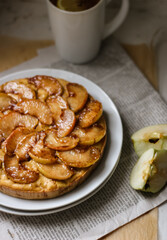 Fresh apple pie on the white plate, the pie is decorated with caramelized apple slices, an appetizing pie on a newspaper background, sweet homemade pastry with apples
