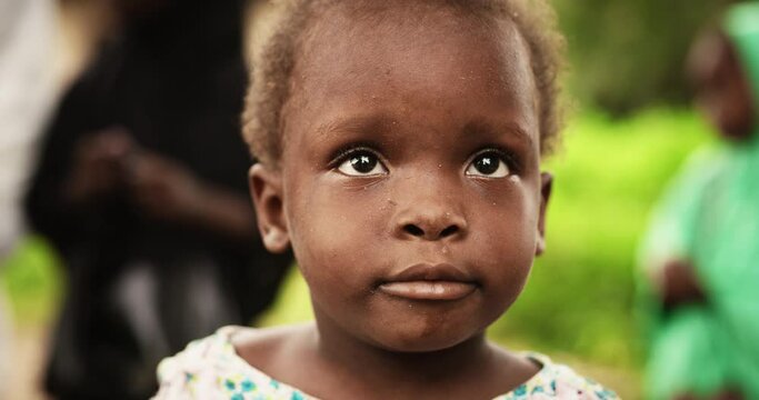 Close Up Portrait of a Cute African Little Todller Smiling at the Camera with Blurred People Moving in the Background. Black Rural Child Representing Hope for a Better Future, a Call for Solidarity 