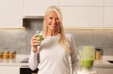 Beautiful woman holding a healthy green smoothie in a kitchen 
