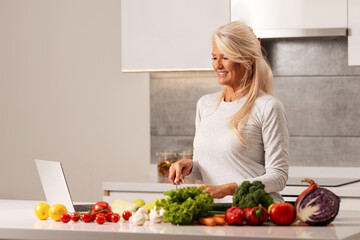 Beautiful woman with laptop, preparing healthy and delicious food in a modern kitchen 
