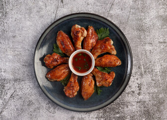 Honey Glazed Chicken Wings with herbs and tomato sauce on a round plate on a dark gray background. Top view, flat lay