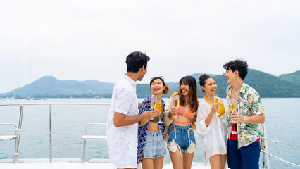 Group of Asian man and woman friends enjoy and fun luxury outdoor lifestyle celebration party drinking champagne together while travel on catamaran boat yacht sailing in the ocean on summer vacation