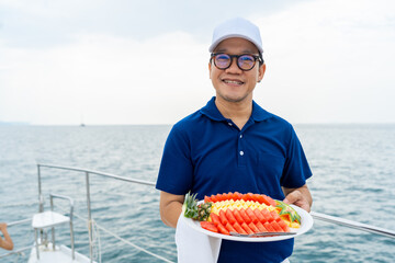 Portrait of Happy Asian man waiter holding fresh fruit on serving dish for serving to passenger...