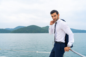 Fototapeta premium Portrait Confident Caucasian businessman relax and enjoy luxury outdoor lifestyle for successful business travel on luxury private catamaran boat yacht sailing in the ocean on summer vacation.