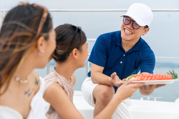 Asian man waiter serving fresh fruit to woman passenger tourist on luxury catamaran boat yacht...