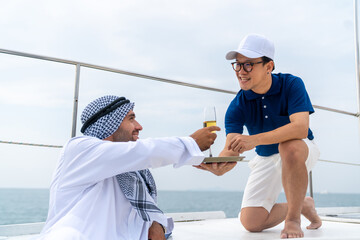 Asian man waiter serving fruit juice to Arab businessman passenger while luxury catamaran boat...