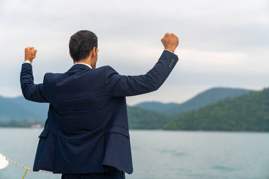 Confident Caucasian Businessman Raise Hand Up With Shouting Celebrating For Global Business Success While Travel On Luxury Private Catamaran Boat Yacht Sailing In The Ocean On Summer Holiday Vacation