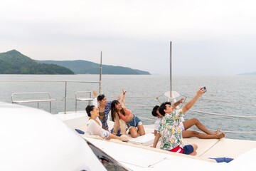 Group of Asian man and woman friends using mobile phone taking selfie together while travel on...