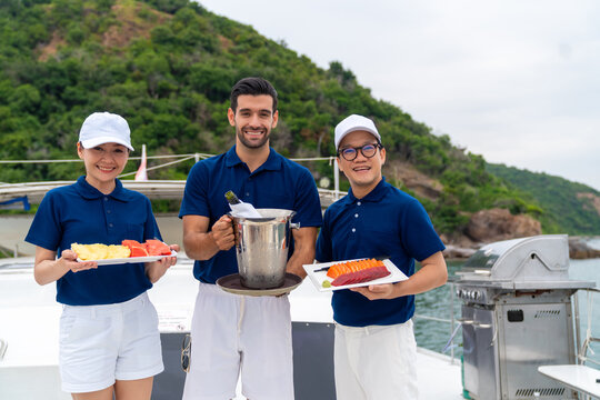 Portrait of Waiter and waitress holding food and drink for serving to passenger tourist travel on luxury private catamaran boat yacht on summer vacation. Cruise ship service occupation concept.