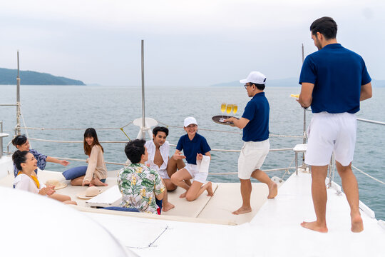 Yacht crew serving fruit and champagne to passenger tourist during celebration party travel on luxury catamaran boat yacht sailing in the ocean on summer vacation. Cruise ship service occupation.