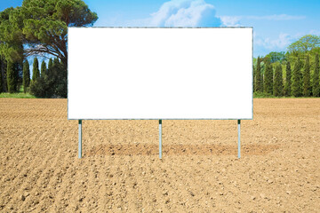 Blank advertising signboard in a plowed agricultural field with trees on background - concept with...