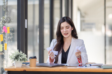 Obraz premium Asian Businesswoman having a tea, sitting on desk in workplace, writing down notes, opened laptop in document the financial report, business plan investment, finance analysis concept.