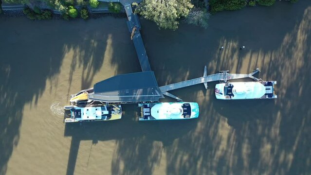 Top down Timelapse drone shot of 2 City Cat Boats leaving dock and driving away on river. Shot in evening sun with long shadows. 3 boats were docked. Shot near UQ, St Lucia, Qld Austalia