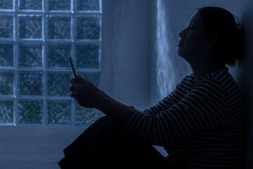 Silhouette depress woman sitting and hold smartphone in hand with moonlight.