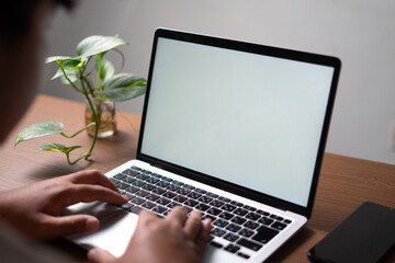 Fototapeta premium Man typing on a laptop with a white blank screen for mockup