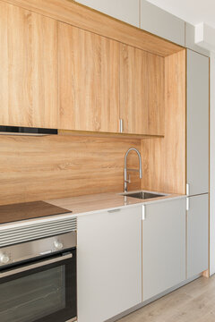 Closeup Of Piece Of Modular Kitchen Furniture Made Of Light Wood. Modern Cozy Kitchen Interior With Appliances Built Into Marble Countertop. Hood Hidden From View In Cabinet Above Stove.