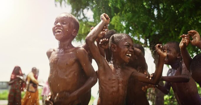 Group of Happy and Innocent Black Children Playing and Enjoying the Blessing of Rain Water After Long Drought. Authentic African Kids Jumping and Laughing when Water Gets Poured on Them.