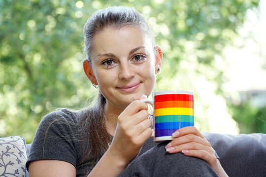 Young pretty woman drinking coffee or tea from mug with rainbow colors