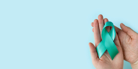 Hands of woman holding Teal ribbon on blue background, Symbolic for cervical cancer, ovarian cancer, gynecological cancer and PCOS. And sexual assault awareness.