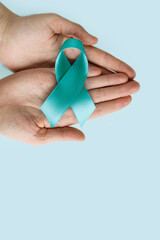 Hands of woman holding Teal ribbon on blue background, Symbolic for cervical cancer, ovarian cancer, gynecological cancer and PCOS. And sexual assault awareness.